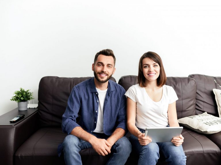 Photo of smiling couple sitting on couch illustrates blog: "2022 Tax Season: How to Avoid Penalties and Interests "
