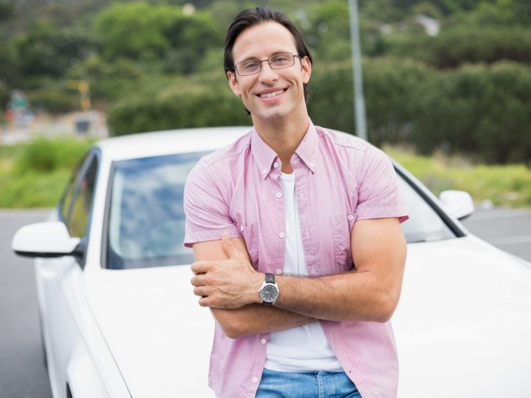 Photo of smiling man leaning against car illlustrates blog: "What Is The IRS Mileage Rate for 2022?"