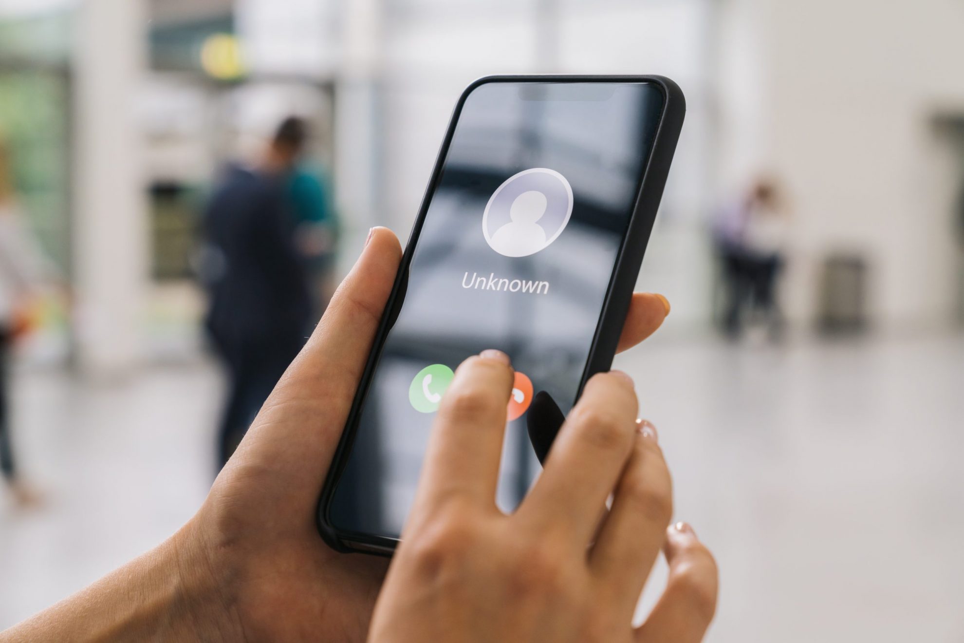 Close-up of woman holding phone that reads "Unknown" illustrates blog: "What To Do If a Scammer Impersonates the IRS?"