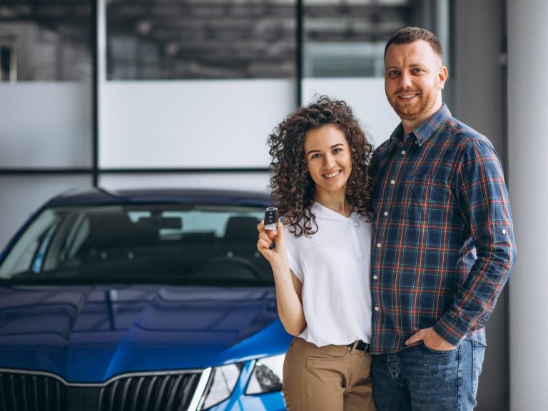 Photo of couple holding keys with car behind them illustrates blog: "Is Auto Insurance Less Expensive if You Are Married?"