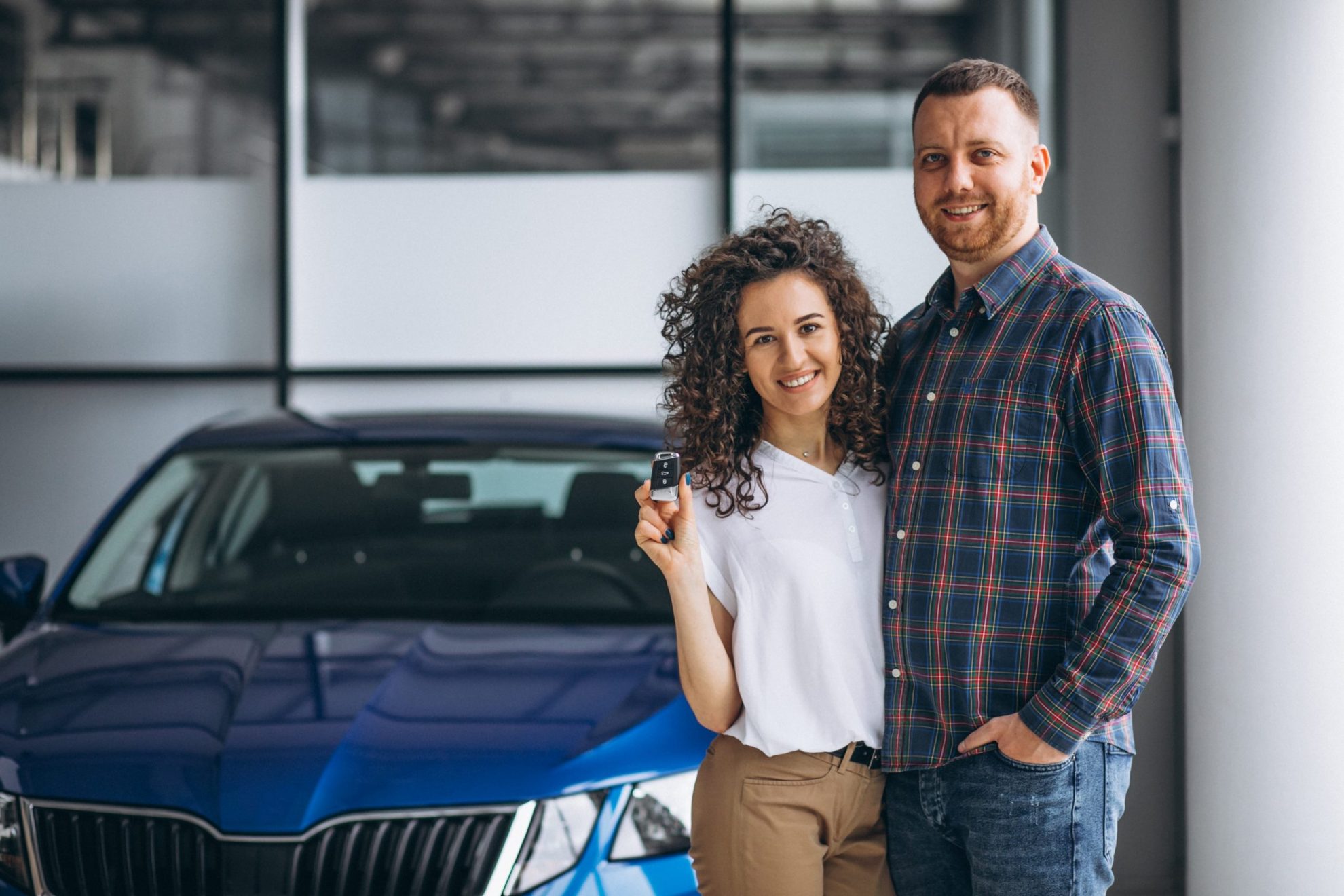 Photo of couple holding keys with car behind them illustrates blog: "Is Auto Insurance Less Expensive if You Are Married?"