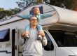 Man carrying child on his shoulders with RV in the background
