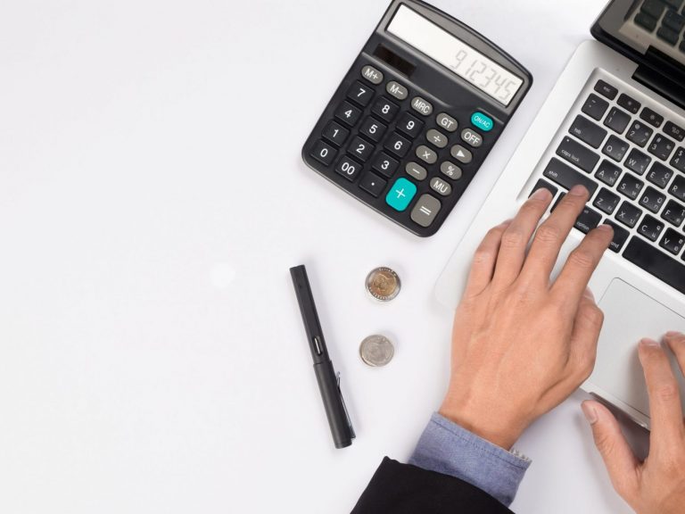 Closeup of person typing on laptop with calculator by their side illustrates blog "Tax Season Tips – How to Make the Process a Little Easier"