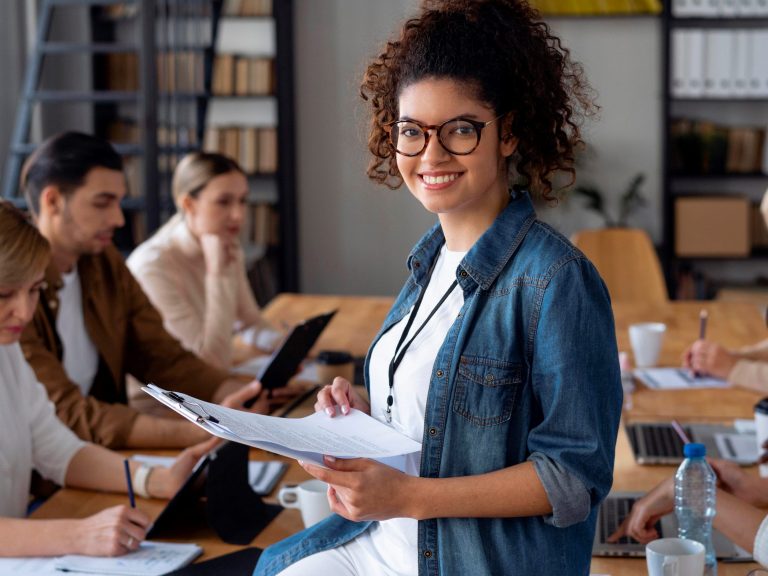 Photo of smiling woman in office illustrates blog "What Is the Difference Between a Business Owners Policy (BOP) and General Liability Insurance (GL)?"