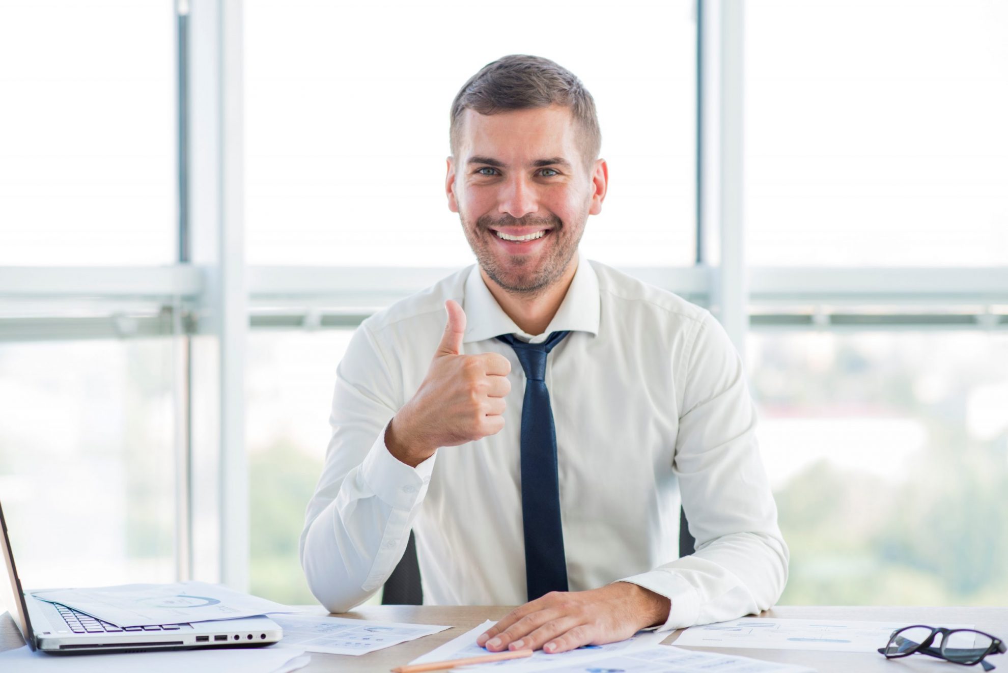 tax-pro-FP Smiling man giving thumbs up behind desk illustrates blog "5 Reasons To Use a Tax Professional"