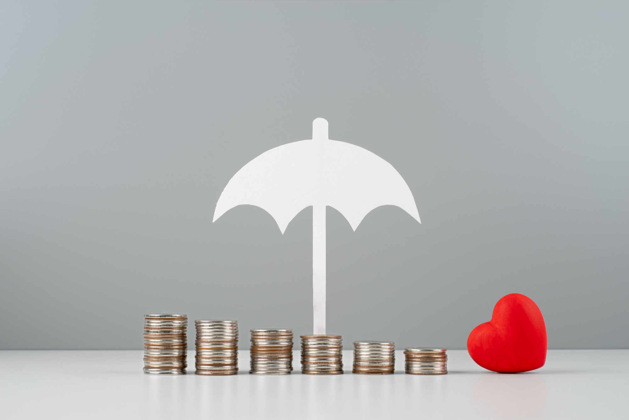 Stacked coins with umbrella and heart symbolizing bundle home and auto insurance protection